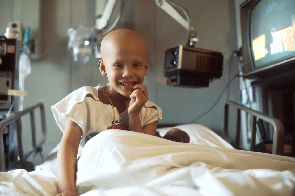 Krebskrankes Kind sitzt im Krankenhausbett und lacht fröhlich 