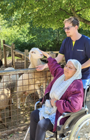 Eine Frau im Rollstuhl streichelt ein Schaf, während ein Mann sie unterstützt.