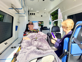 Ein Patient liegt in einem Krankenwagen, während eine Begleitperson ihn betreut.