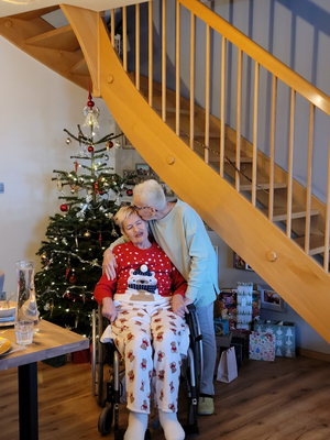 Eine Person umarmt eine andere im Rollstuhl vor einem Weihnachtsbaum.