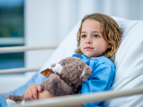 Kind im Krankenhausbett mit Teddybär