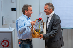 Zwei Männer überreichen sich einen Geschenkkorb in einem geschäftlichen Umfeld.