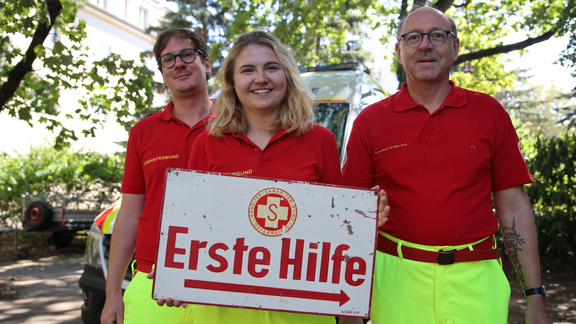 3 Samariter:innen mit Vintage-Hinweisschild 