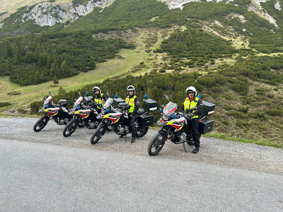Fünf Motorradfahrer in Uniform stehen neben ihren Motorrädern in einer bergigen Landschaft.