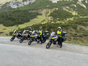 Fünf Motorradfahrer in Uniform stehen neben ihren Motorrädern in einer bergigen Landschaft.